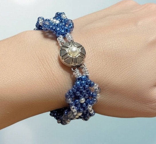 Blue beaded bracelet with a silver clasp on a wrist against a light blue background
